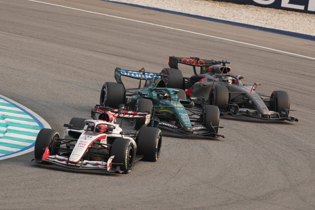 Haas, Aston Martin, and Audi cars following closely around a bend at Sepang Circuit